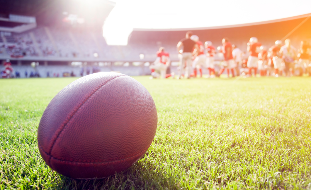 Football on the grass with players huddled on the field at AT&T Stadium in Arlington TX