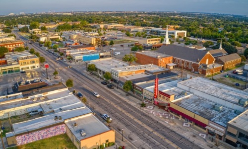 Aerial view of Main Street in downtown Grand Prairie, Texas, showing local shops, historic buildings, and the Texas Theatre under a clear sky.