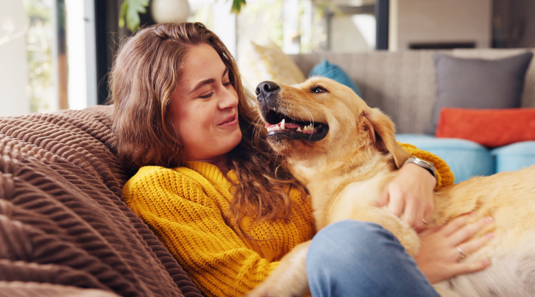 A woman in a yellow sweater cuddling her golden retriever on a couch inside an apartment at Creekside at Grand Prairie.