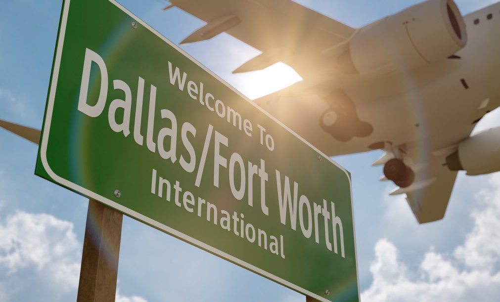 Dallas/Fort Worth International Airport sign with a jet flying above it in the sun.