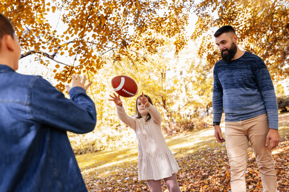 Family playing catch with a football under golden autumn trees in an Arlington TX park